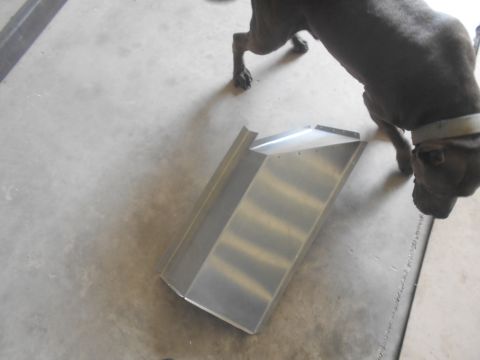 1992 Ford Bronco - A dark-colored dog is sniffing a piece of bent metal on a concrete floor. The metal piece appears to be a custom part with visible rivets.