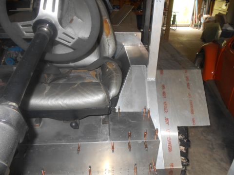 1992 Ford Bronco - The interior of a vehicle build shows a worn leather driver's seat and steering wheel, with unfinished aluminum paneling and rivets visible…