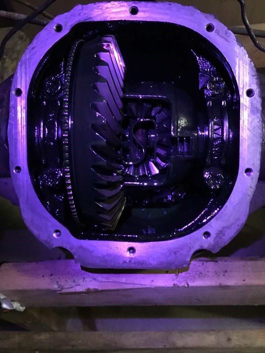 Open differential housing with ring and spider gears, illuminated by purple light.