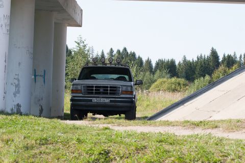 1993 Ford Bronco - A silver Ford Bronco is parked under a concrete overpass with a forest in the background. The vehicle has four auxiliary lights mounted on…