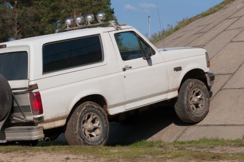 1993 Ford Bronco - A white 1993 Ford Bronco is shown from the side, angled up a concrete embankment. The vehicle has a roof rack with four auxiliary lights an…