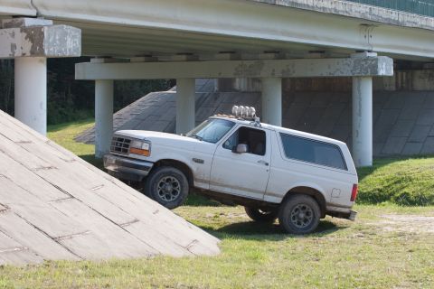 1993 Ford Bronco - A white Ford Bronco is shown at an angle on a grassy incline, with its front wheels on the incline and its rear wheels on flat ground. The…