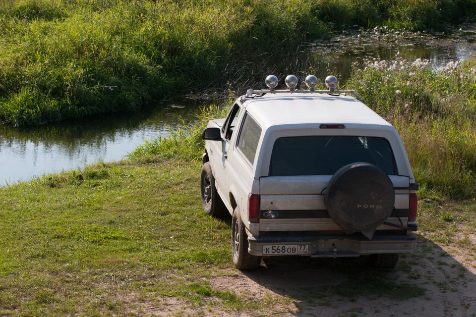 White 1993 Ford Bronco parked by water, rear view, spare tire on back, roof lights