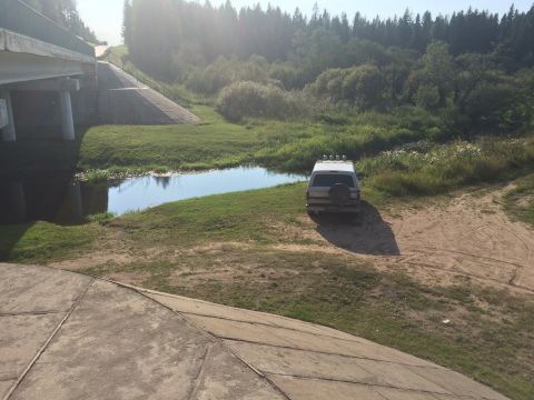 1993 Ford Bronco - A silver SUV is parked on a dirt path next to a small body of water and a grassy embankment. The vehicle is viewed from the rear, with a sp…