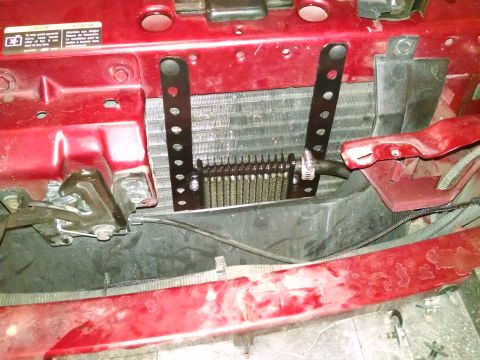 2002 Pontiac Grand Prix - A close-up view of an aftermarket transmission cooler mounted in front of the radiator of a red vehicle. The cooler is secured with black m…