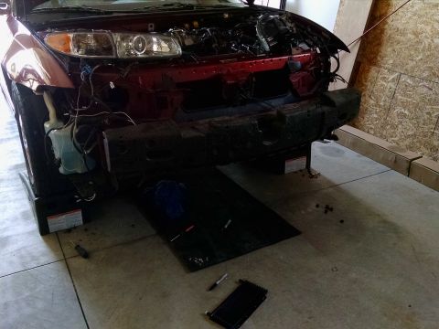 2002 Pontiac Grand Prix - The front end of a dark red Pontiac Grand Prix is shown with the bumper removed, revealing the engine bay and various components. Tools and…