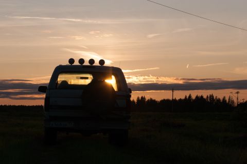 1993 Ford Bronco - The rear view of a dark-colored SUV is silhouetted against a sunset sky, with the sun peeking through the rear window. The vehicle is parke…