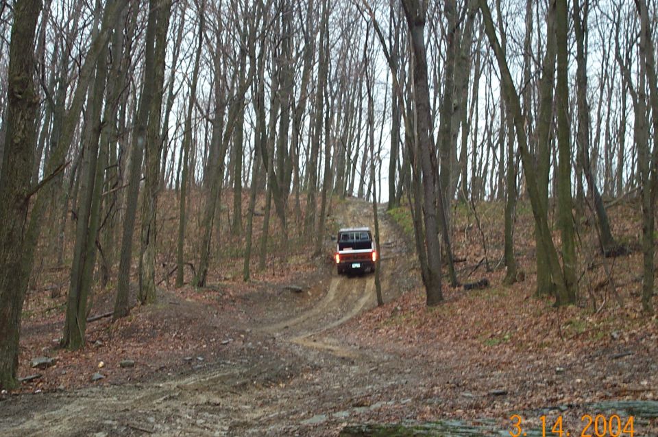 Red and white truck climbing a dirt trail up a wooded hillside of bare trees