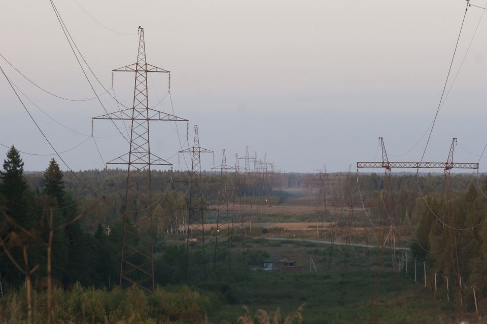 Landscape with multiple power line towers in a wooded and open field setting.