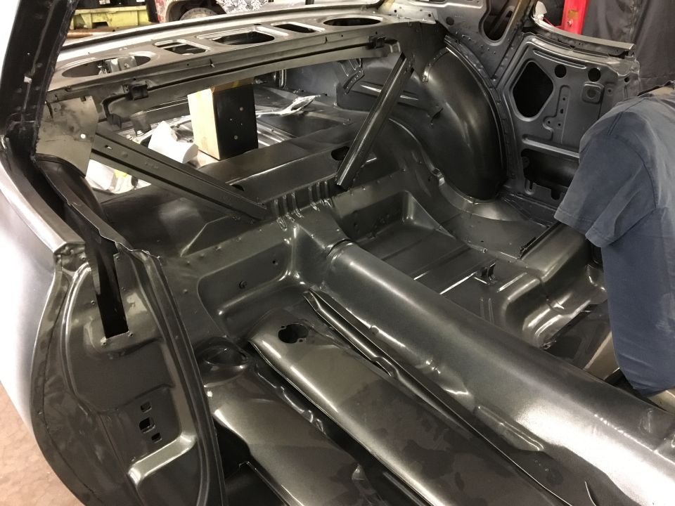 Interior of a classic car, painted dark gray primer, showing floor pans and structural elements.