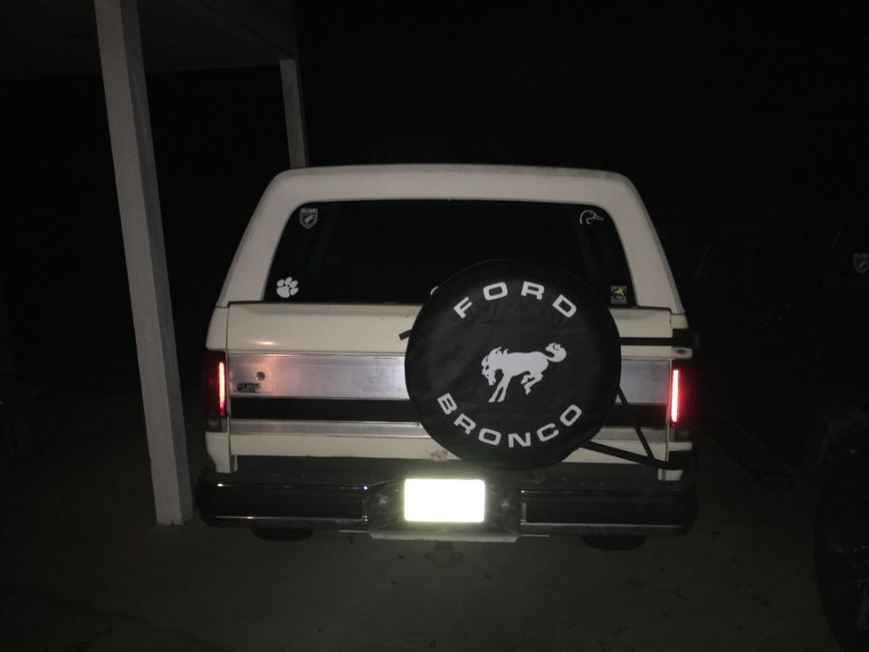 Rear view of a white Ford Bronco with a black spare tire cover displaying a white Bronco graphic and text.