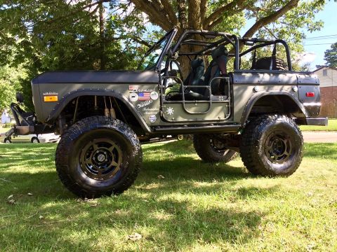 1972 Ford Bronco - A heavily modified olive green 1972 Ford Bronco is parked on a grassy lawn under a large tree. The off-road vehicle features large tires, a…