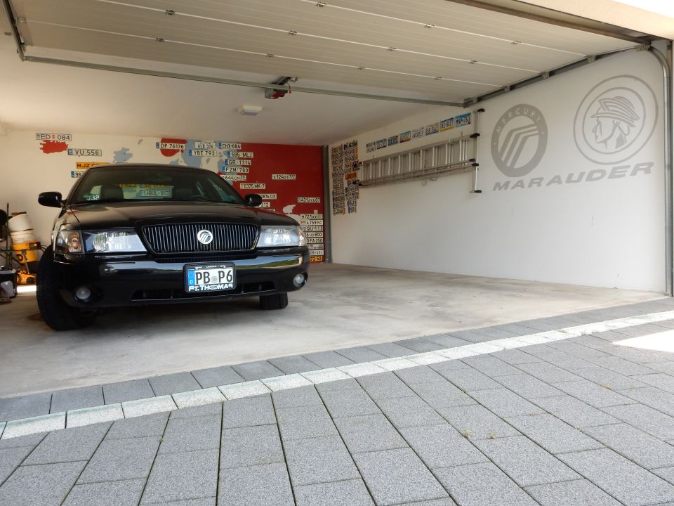 Black 2003 Mercury Marauder parked in a garage with a ladder and license plates on the wall