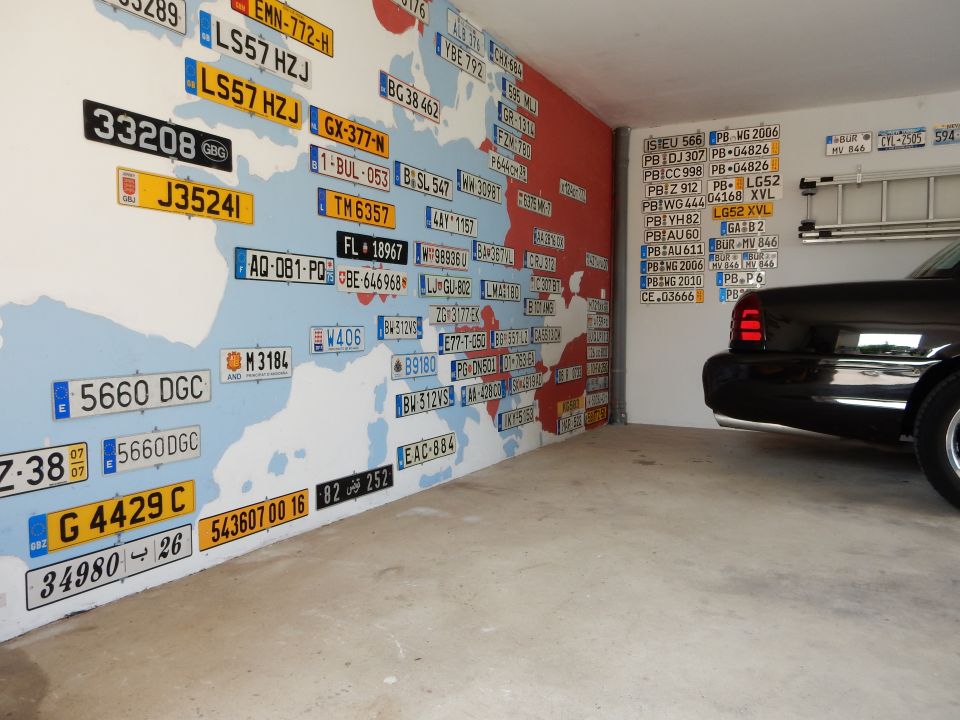 Black sedan, possibly a 2003 Mercury Marauder, parked in a garage with a wall mural of license plates and a world map