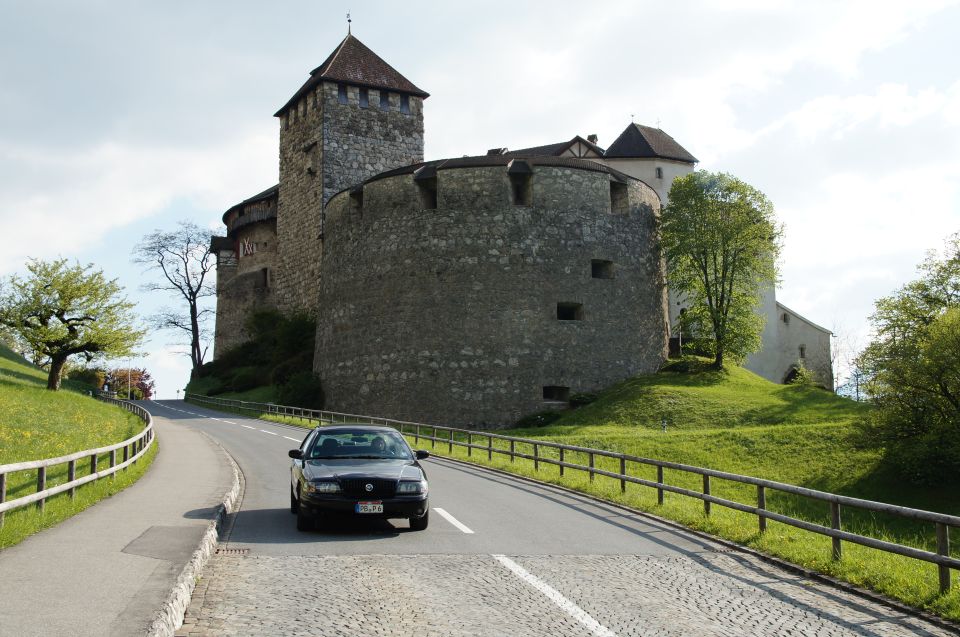 Black sedan drives on a road towards a stone castle