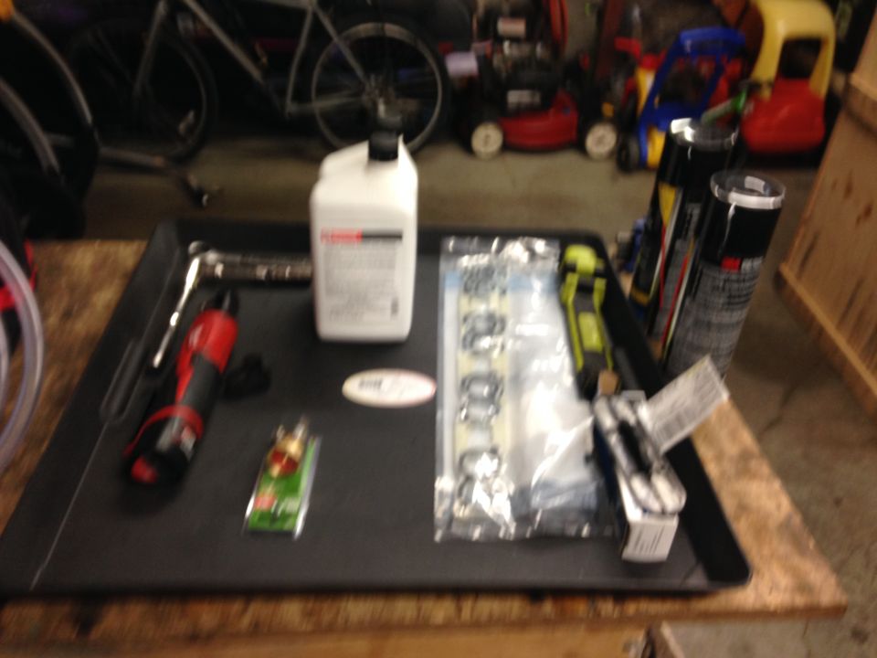 Tray with a bottle of fluid, a wrench, a drill, a small green item, a package of gaskets, and spray cans