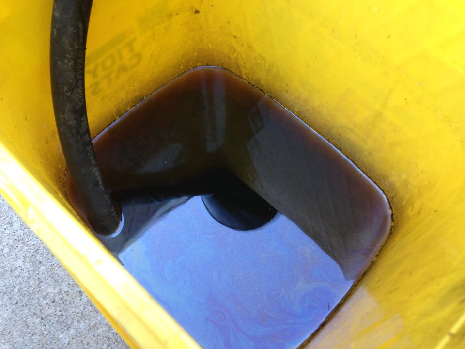 Yellow bucket with dark used oil and a black hose. Supermotors.net logo at bottom right