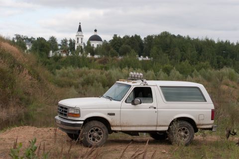 1993 Ford Bronco - A white 1993 Ford Bronco is parked on a dirt path, with a church visible on a hill in the distance.