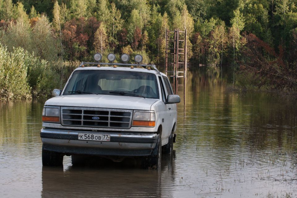 White 1993 Ford Bronco driving through flooded area with trees in background