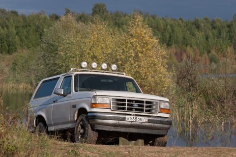 1993 Ford Bronco - A white 1993 Ford Bronco with roof lights sits parked near a body of water and trees.