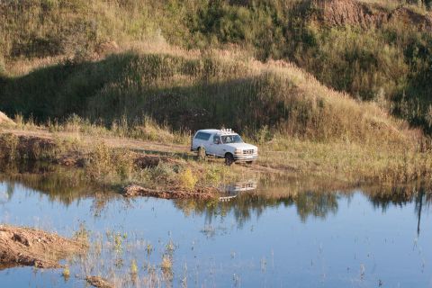 1993 Ford Bronco - A white 1993 Ford Bronco is seen off-roading on a dirt path beside a lake.