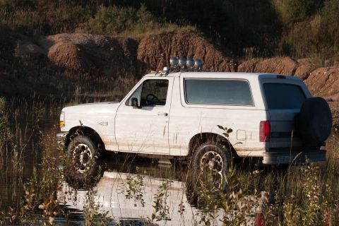 1993 Ford Bronco - This 1993 Ford Bronco is captured in a side profile, partially submerged in shallow water, highlighting its off-road capabilities.
