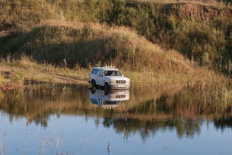 1993 Ford Bronco - A white 1993 Ford Bronco navigates through shallow water, its reflection shimmering on the surface.