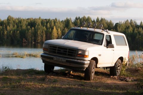 1993 Ford Bronco - White Ford Bronco parked off-road near a lake with a forest backdrop.