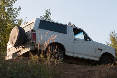 1993 Ford Bronco - A white 1993 Ford Bronco is shown from a low angle, climbing a dirt hill with dry grass in the foreground.