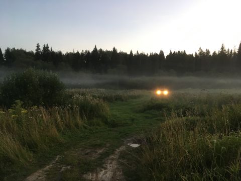 1993 Ford Bronco - A vehicle drives through a foggy field at dusk, its headlights cutting through the mist.