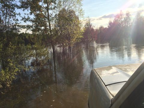 1993 Ford Bronco - Vehicle navigates through flooded terrain with trees reflected in the water under a bright sky.