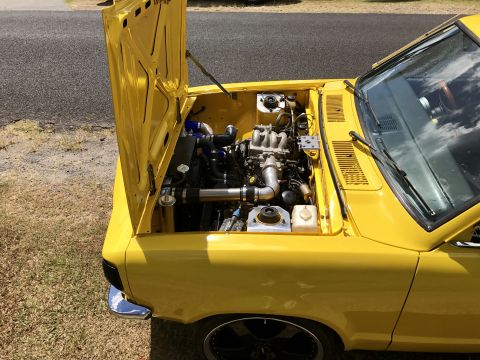 1973 Mazda RX-3 - The engine bay of a yellow car is open, revealing the engine and its components.