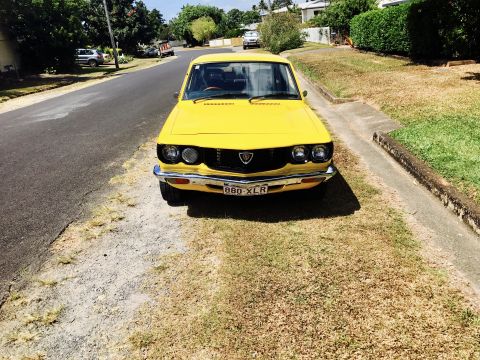 1973 Mazda RX-3 - A bright yellow 1973 Mazda RX-3 coupe is parked curbside on a sunny day.