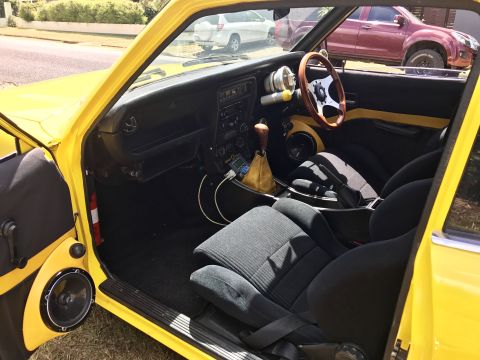 1973 Mazda RX-3 - Interior view of a yellow car aftermarket modifications like a wooden steering wheel and additional gauges.