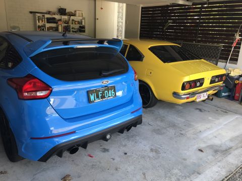 1973 Mazda RX-3 - A yellow 1973 Mazda RX-3 coupe is parked next to a blue Ford Focus RS in a garage.