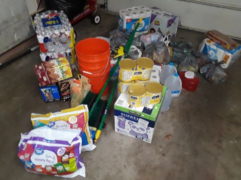 1996 Ford Bronco - A variety of household supplies are organized on a garage floor, including drinks, food, and cleaning tools.
