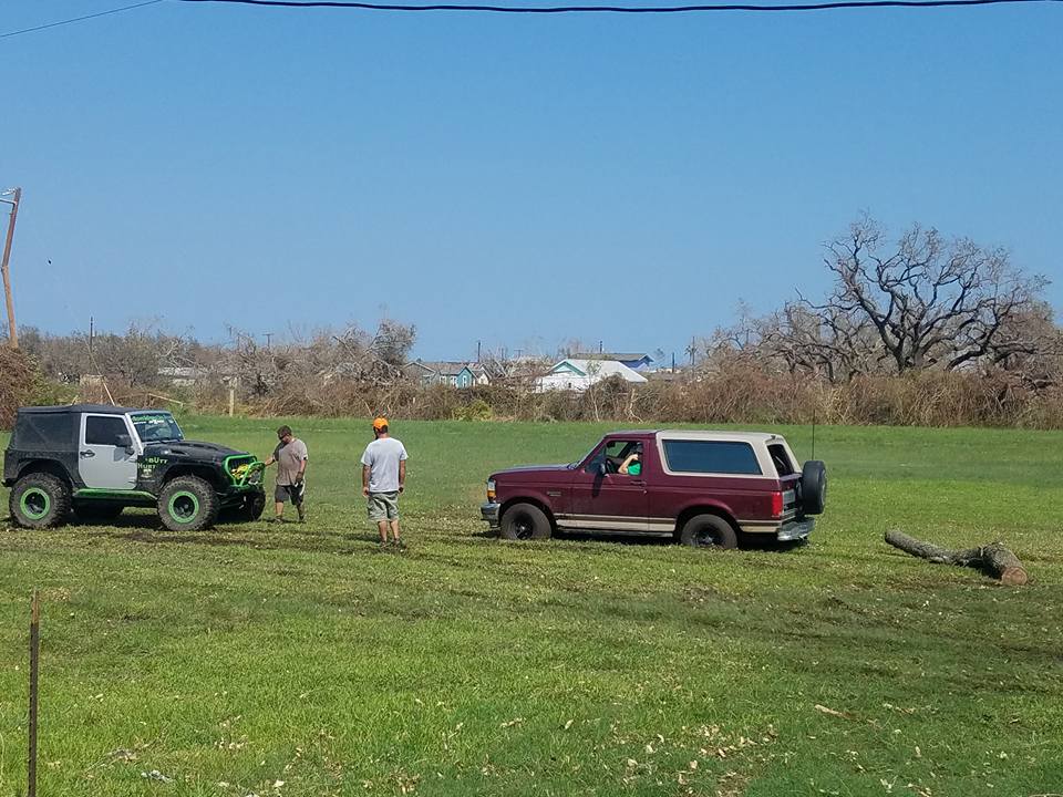 Maroon Ford Bronco and black Jeep Wrangler parked in a grassy field with two men standing nearby