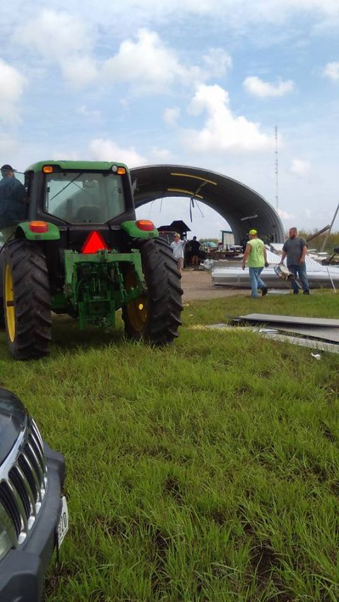 1996 Ford Bronco - A green tractor is seen from the rear, with people and debris around a damaged building under a cloudy sky.