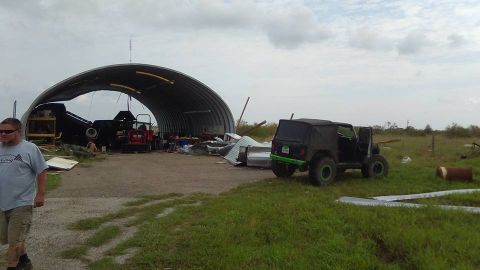 1996 Ford Bronco - A black Jeep Wrangler sits outside a damaged Quonset hut, with a man walking in the foreground.