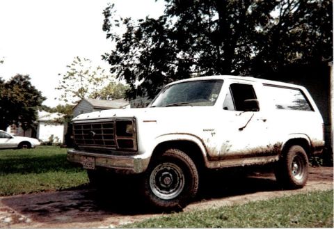 1996 Ford Bronco - A white Ford Bronco is parked on a dirt driveway next to a grassy lawn.