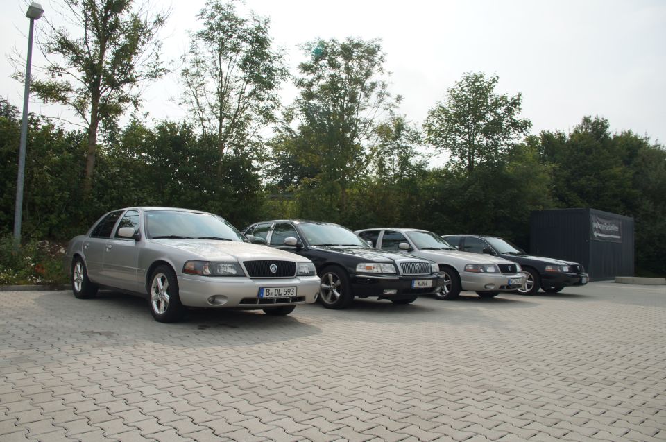 Four Mercury Marauder sedans parked in a lot. The front car is silver, the next two are black, and the last is silver. License plate on front car reads B-DL 593