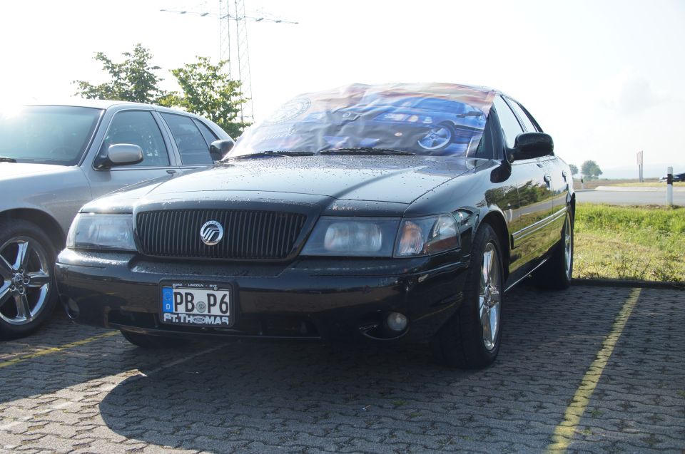 Black 2003 Mercury Marauder parked next to a silver car. Windshield has a cover with car images