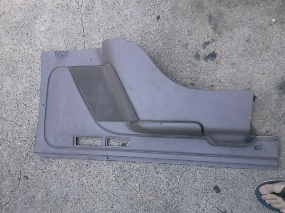 Gray plastic car door panel with armrest and speaker grille cutout, lying on concrete