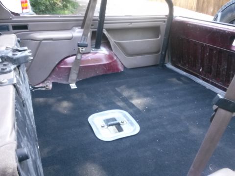 1996 Ford Bronco - The rear cargo area of a 1996 Ford Bronco shows black carpeting and a metal access panel.