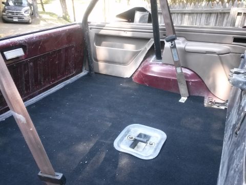1996 Ford Bronco - The rear interior of a vehicle shows dark carpeting and maroon side panels, with a metal latch on the floor.
