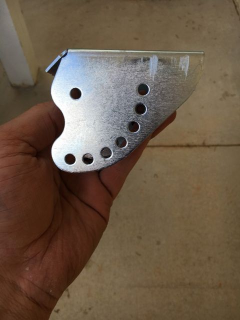 1988 Ford Bronco - A person holds a metal bracket with several holes, likely a vehicle part.