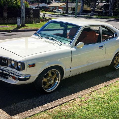 1973 Mazda RX-3 - A white coupe with aftermarket wheels is parked on the side of a residential street.