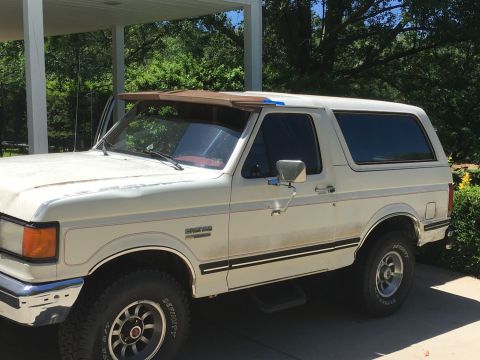 1988 Ford Bronco - A white Ford Bronco with a brown visor is parked outside under a covered area.