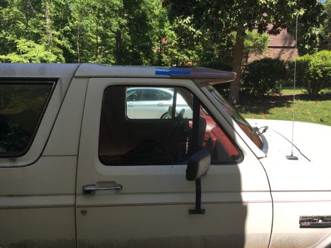 1988 Ford Bronco - Side profile of a white 1988 Ford Bronco, showing its red interior and a sun visor above the windshield.