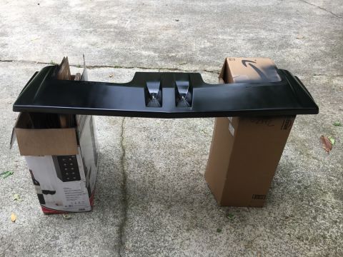 1988 Ford Bronco - A black plastic car part is supported by cardboard boxes on a concrete surface.